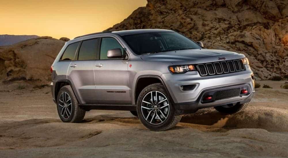 A silver 2018 Jeep Grand Cherokee Trailhawk is parked off-road at sunset.