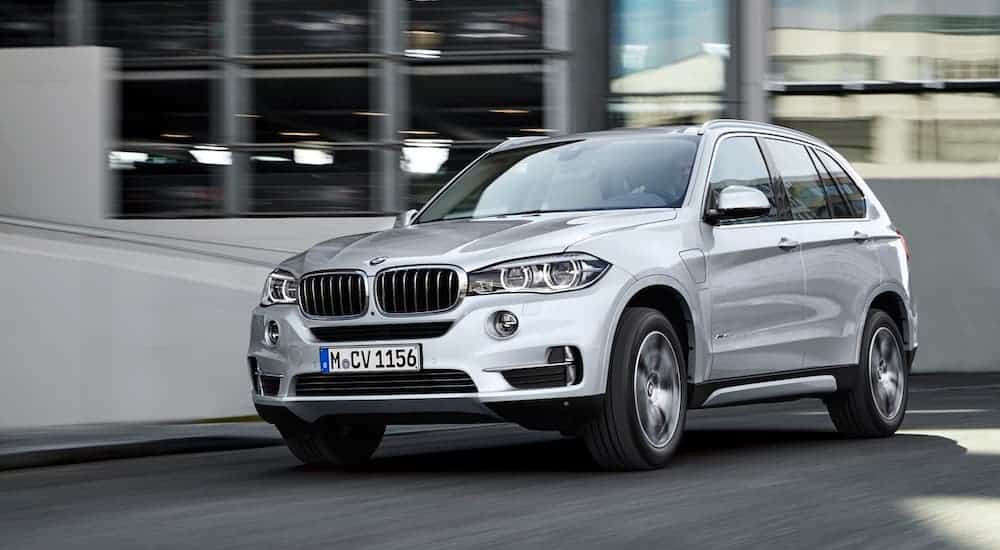 A silver 2015 BMW X5 is driving past city buildings.