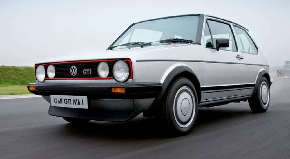 A silver 1976 Volkswagen Golf GTI is shown driving.