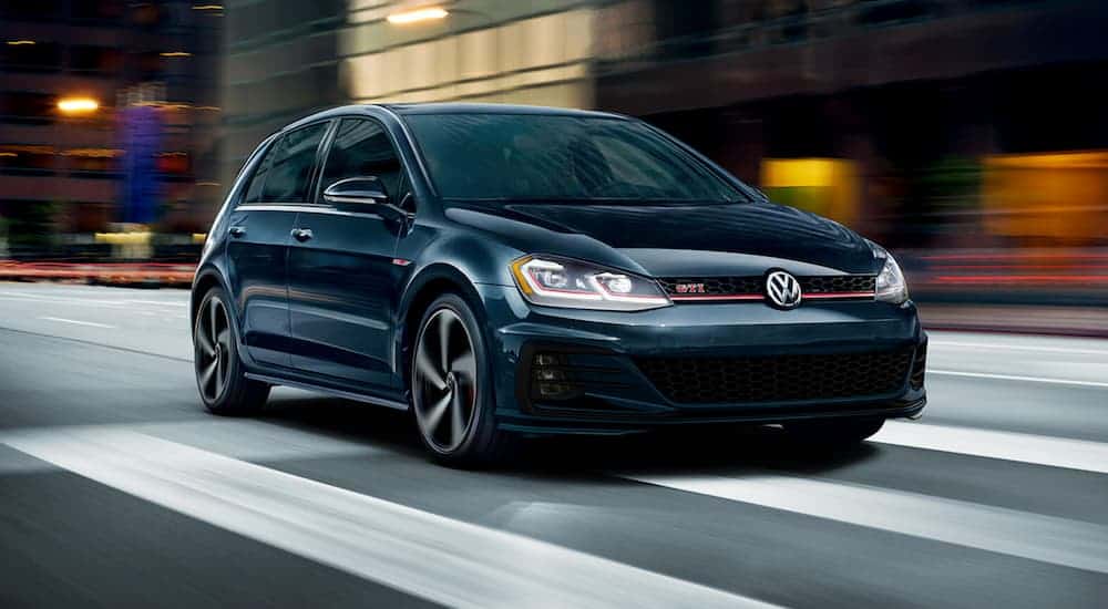 A dark blue 2020 Volkswagen Golf GTI is driving in the city at night.