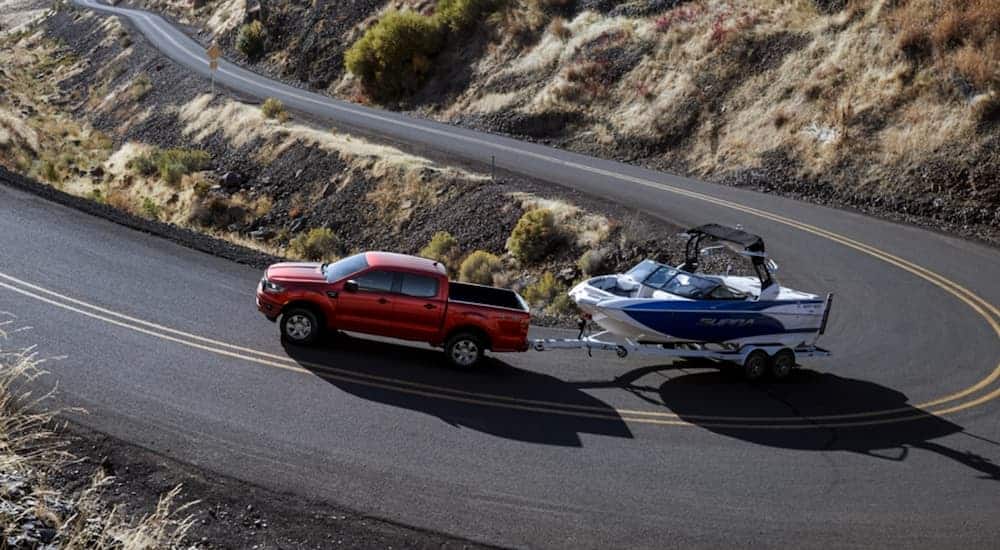 A red 2020 Ford Ranger is towing a boat around a corner up a hill.