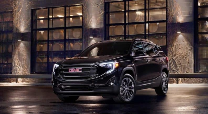 A black 2020 GMC Terrain, which wins when comparing the 2020 GMC Terrain vs 2020 Jeep Compass, is parked in front of a distillery at night.