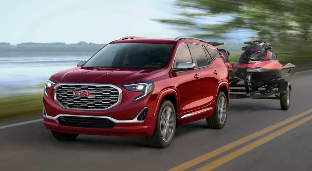 A red 2020 GMC Terrain is towing jet skis past a lake.