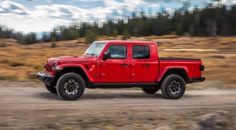 A red 2020 Jeep Gladiator is driving past a blurred field after winning the 2020 Jeep Gladiator vs 2020 Ford Ranger comparison.