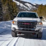 A white 2021 GMC Canyon AT4 is shown driving on a snowy road from the front.