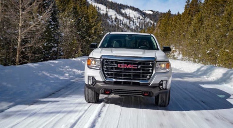 A white 2021 GMC Canyon AT4 is shown driving on a snowy road from the front.