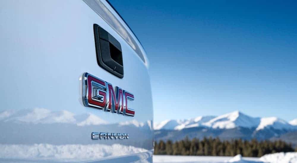 A closeup is shown of a 2021 GMC Canyon AT4 tailgate badging with reflections of snowy mountains.