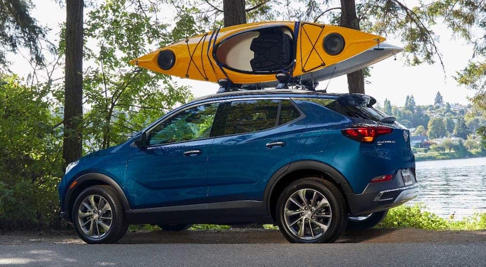 One of the newer Buick SUVs, a 2020 Buick Encore GX is parked next to a lake with a yellow kayak on the roof.