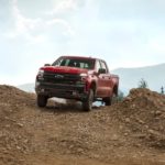 A red 2020 Chevy Silverado Trailboss is driving over a dirt hill against a blue sky.