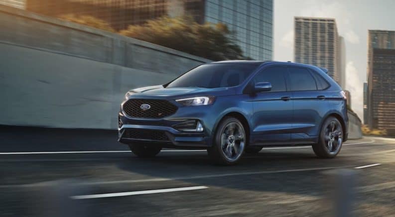 A blue 2020 Ford Edge ST is driving through a city after winning the 2020 Ford Edge vs 2020 Kia Sorento comparison.