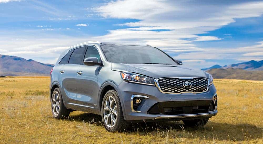 A grey/blue 2020 Kia Sorento is parked in a field with mountains behind it.