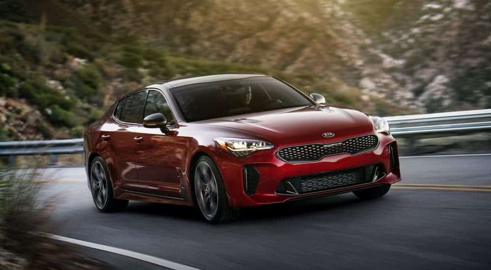 A red 2018 Kia Stinger is driving around corner with a blurred background.