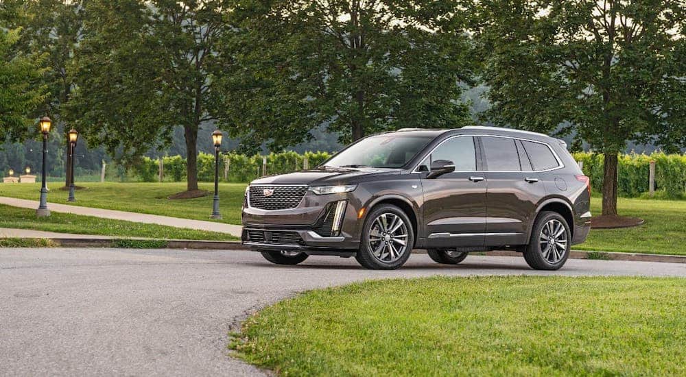 A brown 2020 Cadillac XT6 Premium Luxury is parked in front of a park and trees.