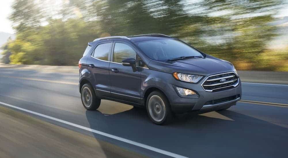 A blue 2020 EcoSport is driving on a tree-lined road after losing the 2020 Chevy Trax vs 2020 Ford EcoSport comparison.