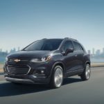 A dark gray 2020 Chevy Trax is driving on a highway leaving a city.