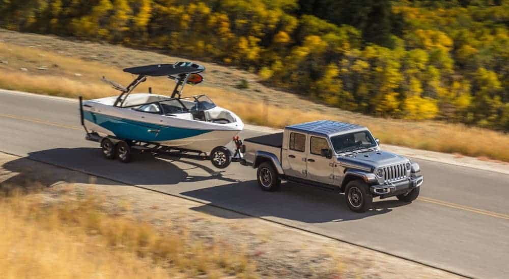 A silver 2020 Jeep Gladiator with a hard top is towing a boat along a highway and shown from a high angle.