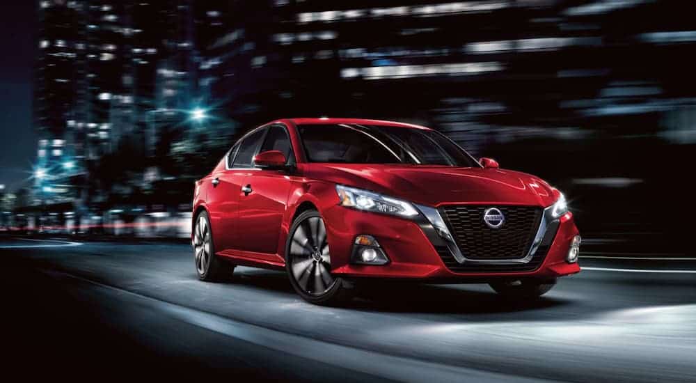 A red 2020 Nissan Altima is driving through a city at night.
