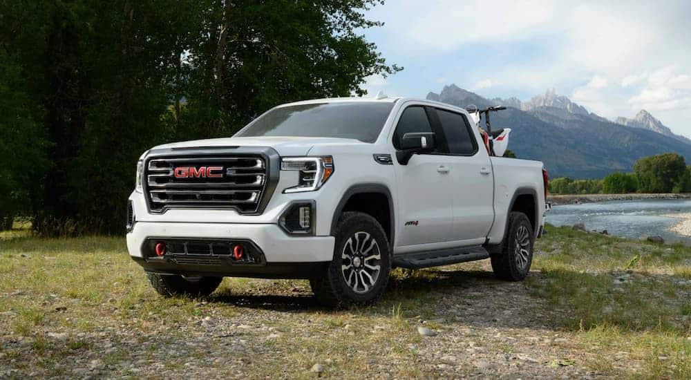 A white 2020 GMC Sierra 1500 AT4 is parked at a lake with mountains in the distance.