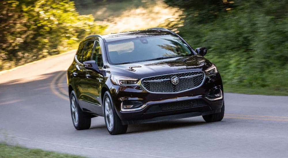A black 2020 Buick Enclave Avenir is driving on a tree-lined road after winning the 2020 Buick Enclave vs 2020 Nissan Pathfinder comparison.