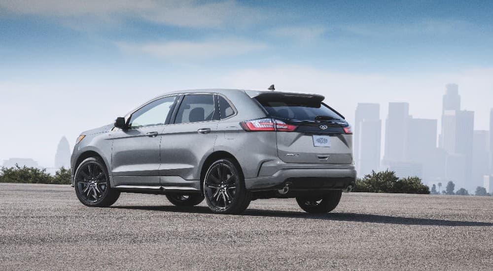 A silver 2020 Ford Edge is parked in an empty lot with a city skyline in the distance.