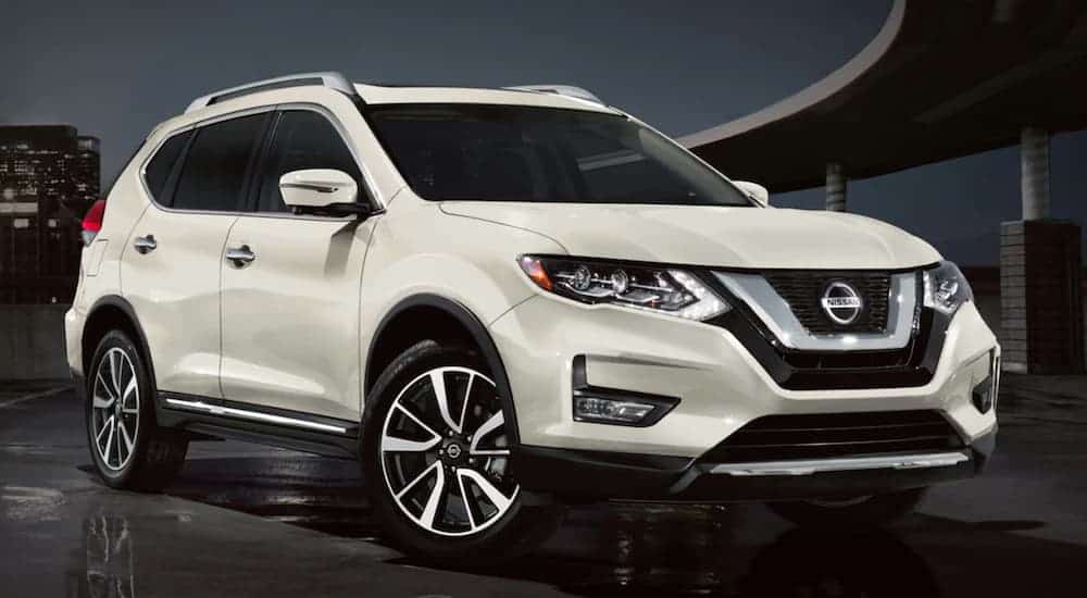 A white 2020 Nissan Rogue is parked in front of a city highway at night.