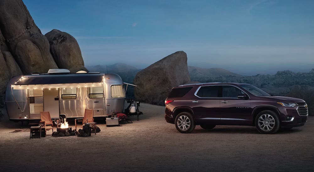 A purple 2020 Chevy Traverse is at a desert campsite with a silver camping trailer.