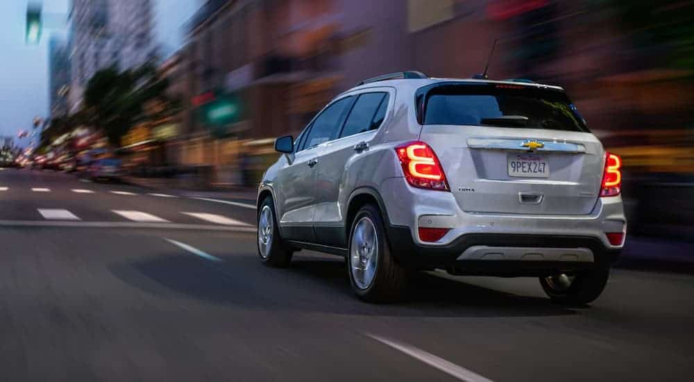 A white 2020 Chevy Trax is driving on a city street at dusk.