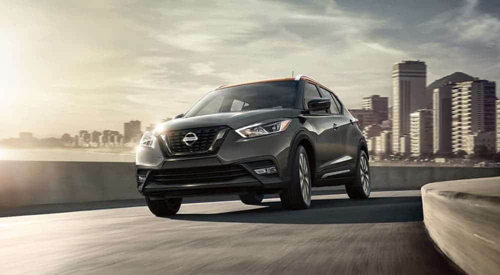 A grey 2020 Nissan Kicks is driving away from a city.