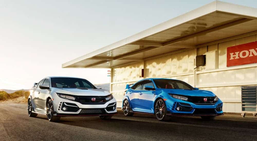 A silver and a blue 2020 Honda Civic Type R are in front of a desert building with a Honda sign on it.