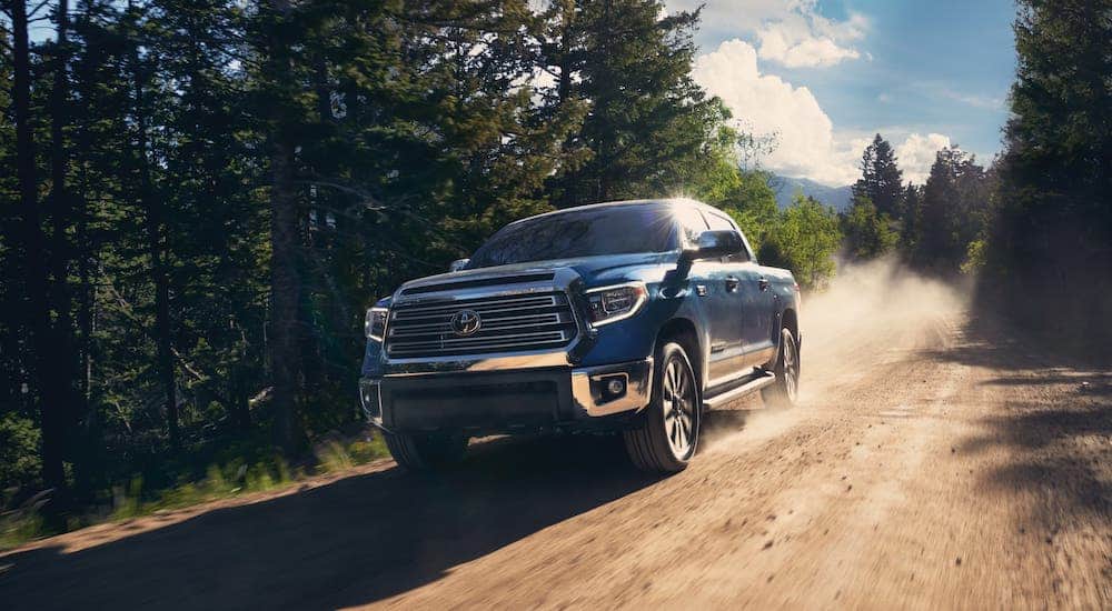 A. blue 2020 Toyota Tundra is driving on a dirt road in the woods.