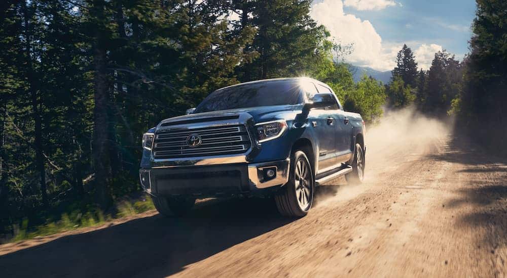 A blue 2020 Toyota Tundra is driving down a dirt road past trees.