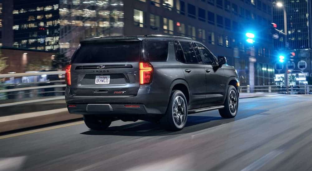 A grey 2021 Chevy Tahoe is driving on a city street at night.