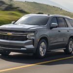 A grey 2021 Chevy Tahoe is driving past grassy hills.