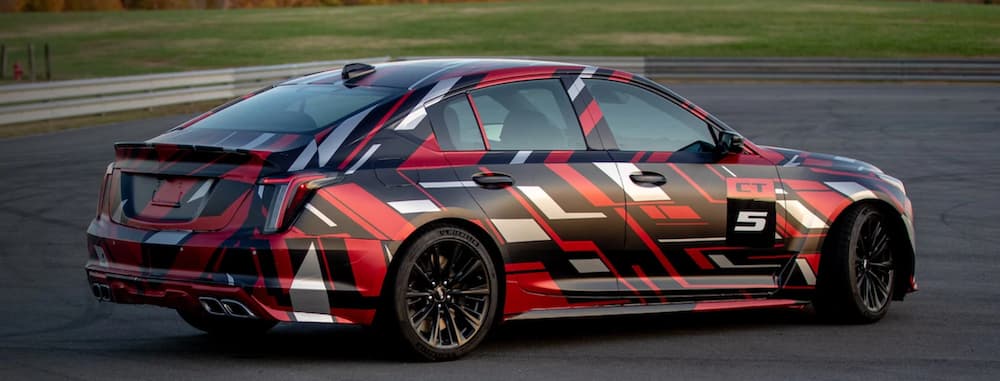 A 2021 Cadillac CT5-V Blackwing with a red, white, and black design on it is racing around a track.