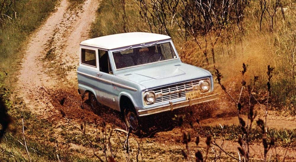 A blue 1967 Ford Bronco is driving on a dirt trail.