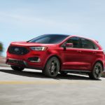 A red 2020 Ford Edge ST is driving around a corner with a city skyline in the distance.