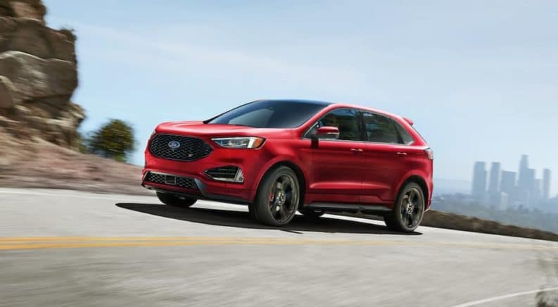 A red 2020 Ford Edge ST is driving around a corner with a city skyline in the distance.
