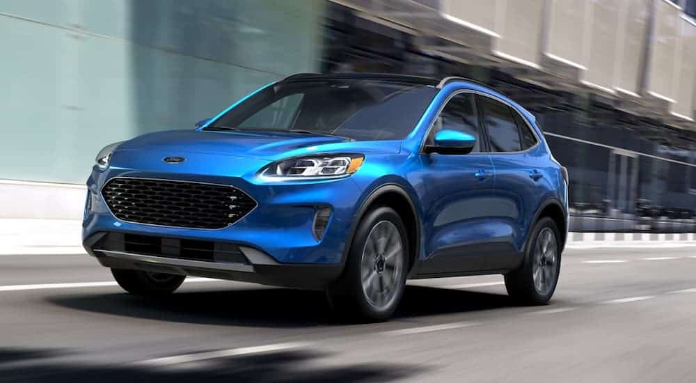 A blue 2020 Ford Escape is driving past an office building.