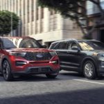 Two Ford SUVs, a red and a grey 2020 Ford Explorer, are driving side by side down a city street.