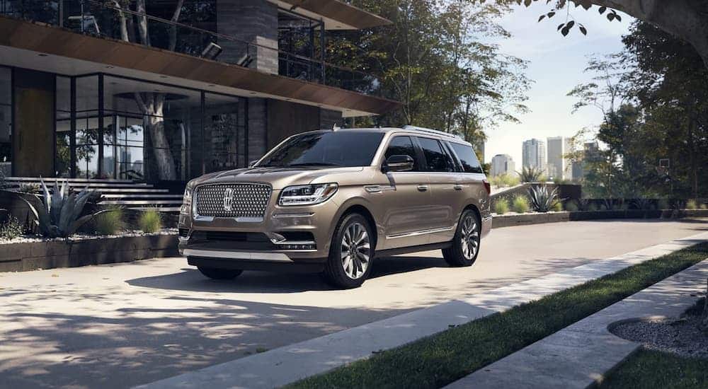 A gold 2020 Lincoln Navigator is parked in front of a modern home.