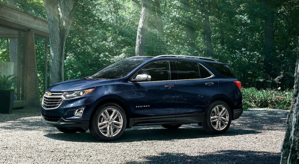 A blue 2020 Chevy Equinox is parked in parked in front of a house in the woods.