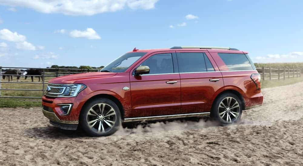 A red 2020 Ford Expedition is driving in the dirt on a farm.
