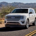 A white 2020 Ford Expedition King Ranch is driving on a desert highway.