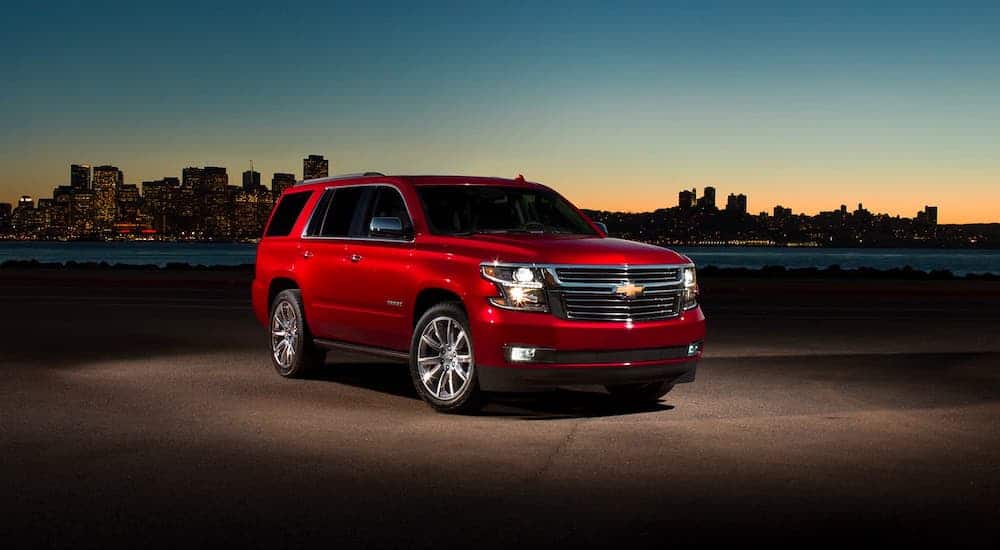 A red 2020 Chevy Tahoe is parked in front of a city skyline at sunset.