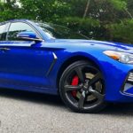A blue 2020 Genesis G70 is shown parked in front of trees angled to the right.