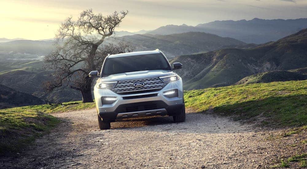 A silver 2020 Ford Explorer is shown from the front on a dirt road with mountains and a tree in the distance.