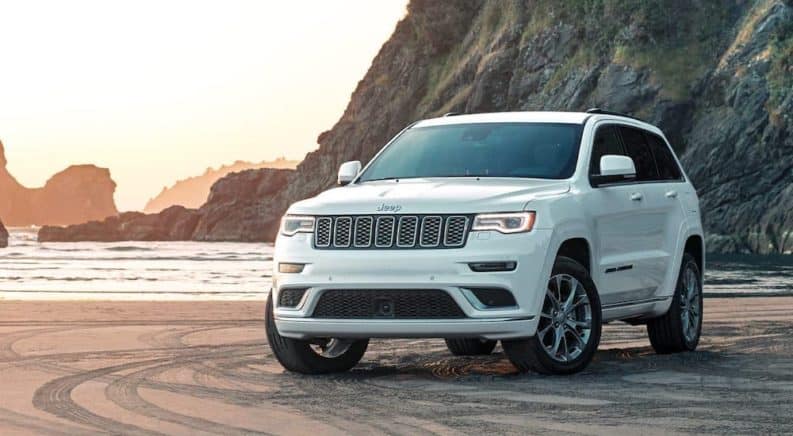 A white 2020 Jeep Grand Cherokee is parked on a beach at sunset after winning the 2020 Jeep Grand Cherokee vs 2020 Ford Explorer comparison.