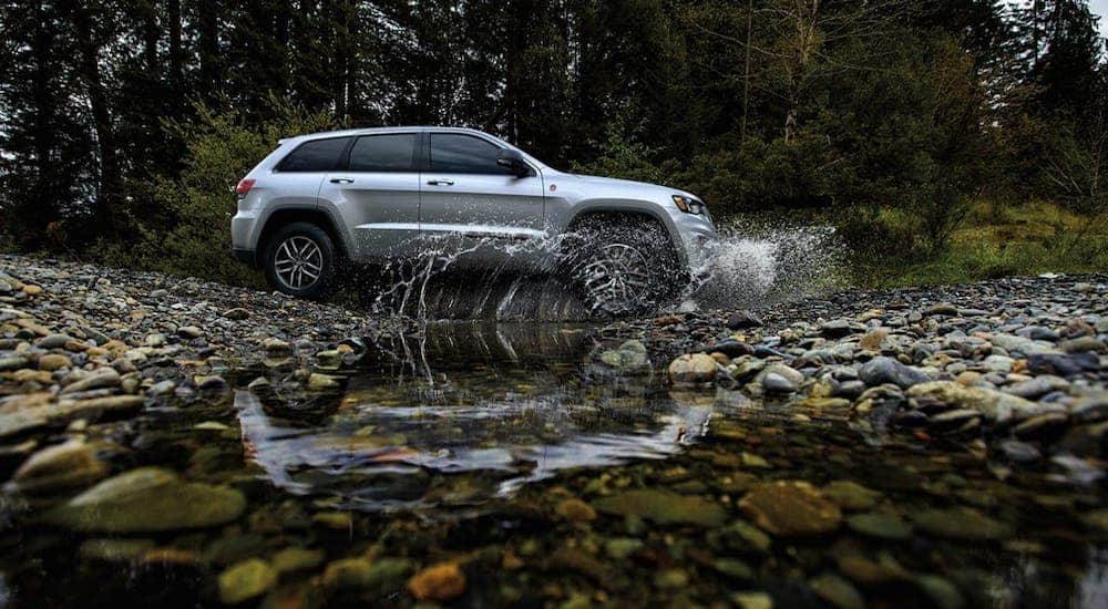 A silver 2020 Jeep Grand Cherokee is shown from the side crossing a river in the woods.