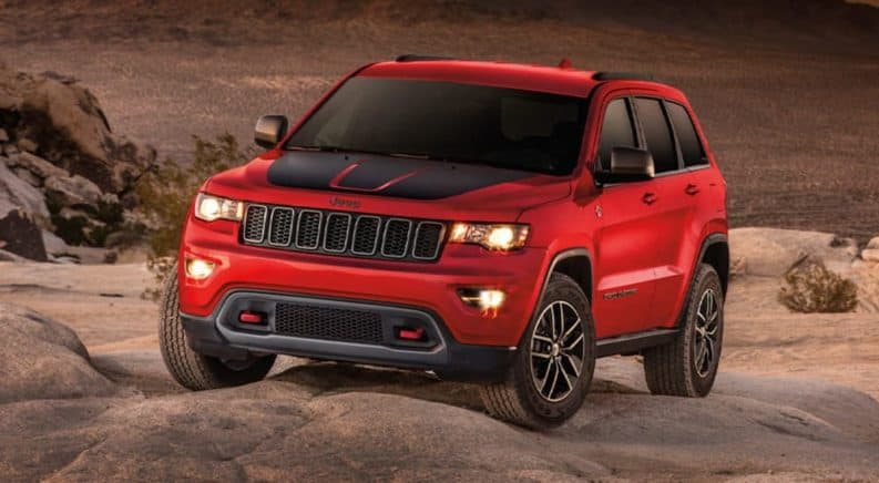 A red 2020 Jeep Grand Cherokee is parked on desert rocks at sunset.