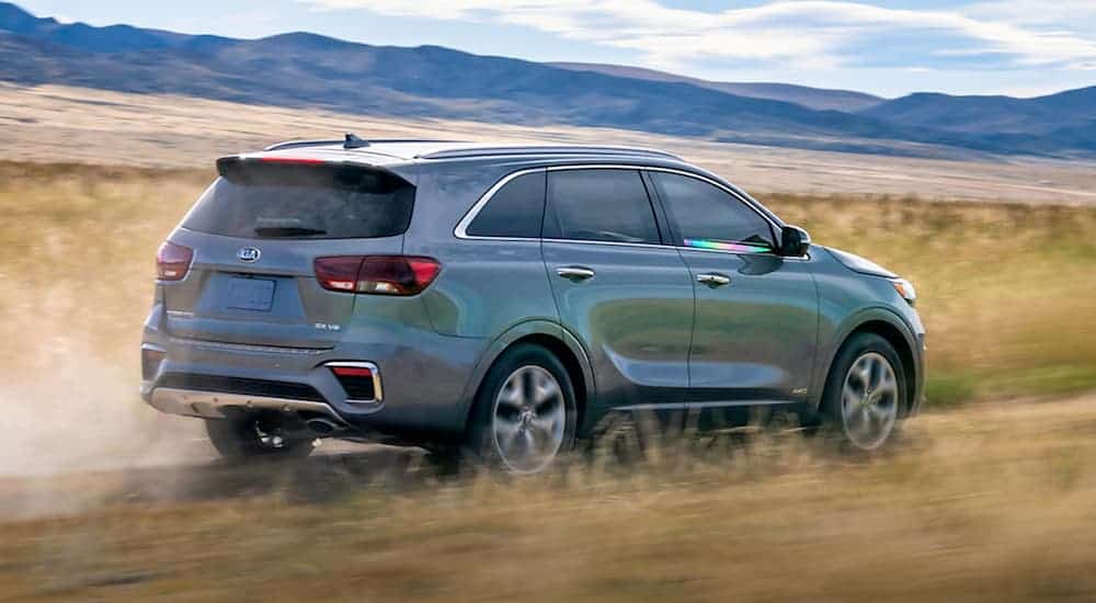 A grey 2020 Kia Sorento is driving on a dirt road with distant mountains.